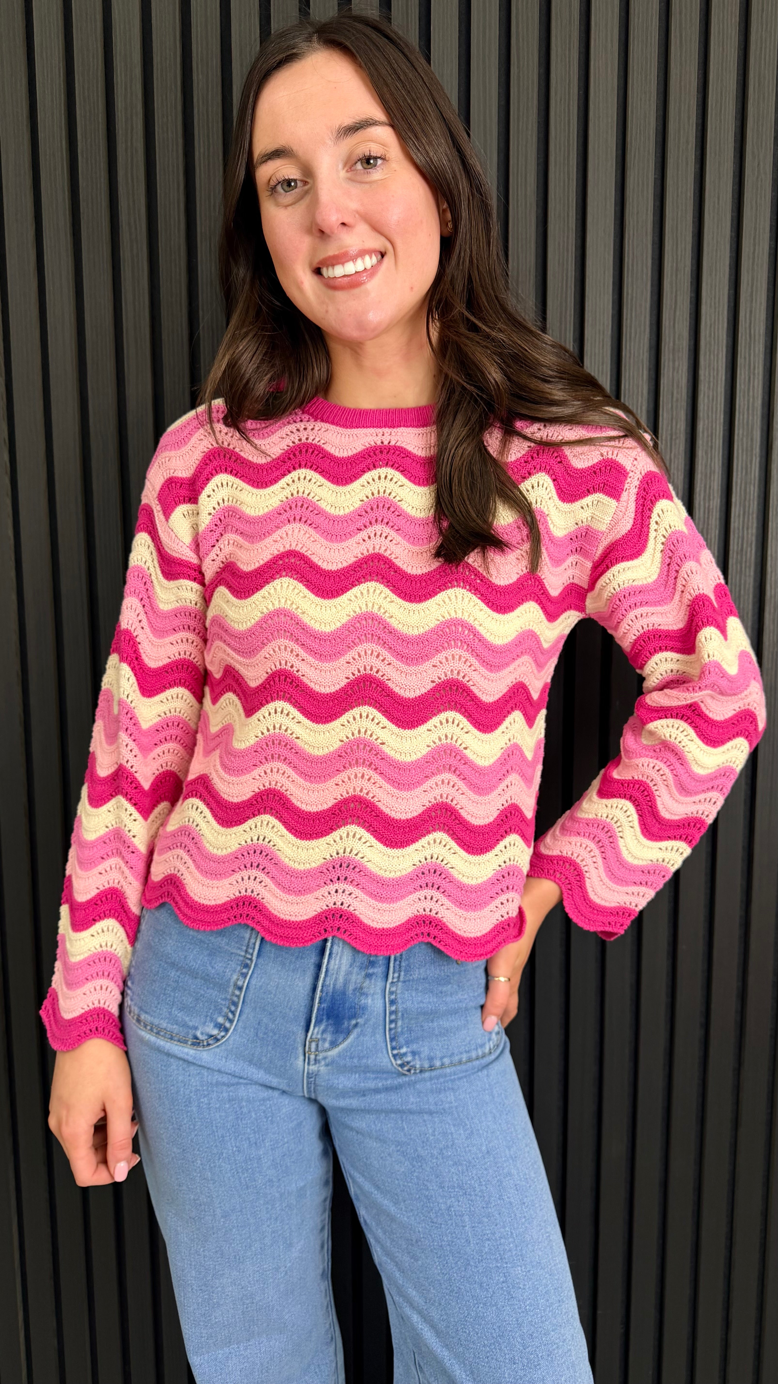 Close up woman wearing a pink and cream zigzag knit jumper styled with blue jeans.