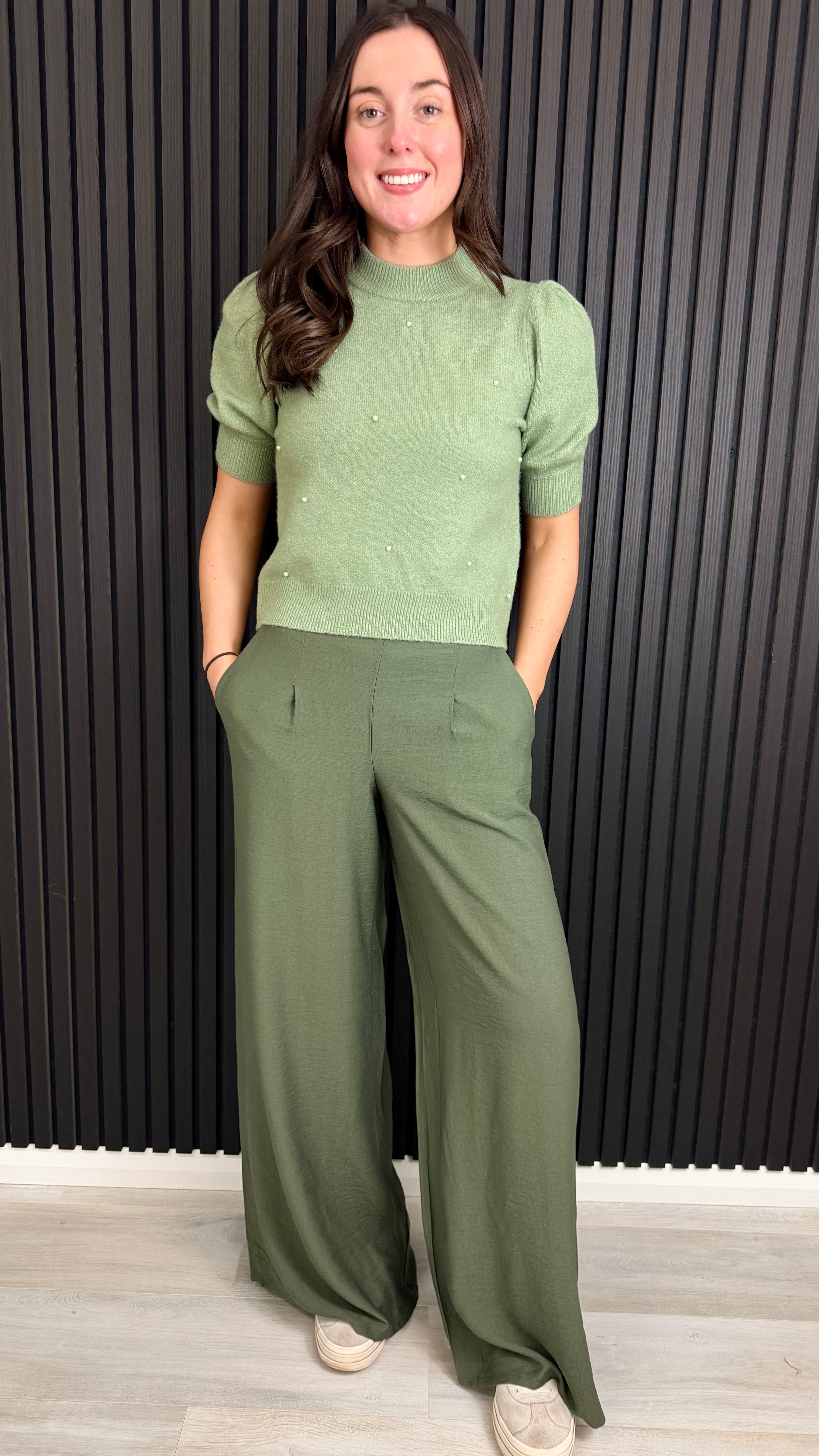 Full outfit Woman wearing a sage green short-sleeve knit top with pearl detailing.
