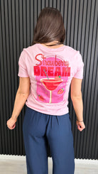 Back view of pink Strawberry Dream graphic t-shirt worn with navy trousers.
