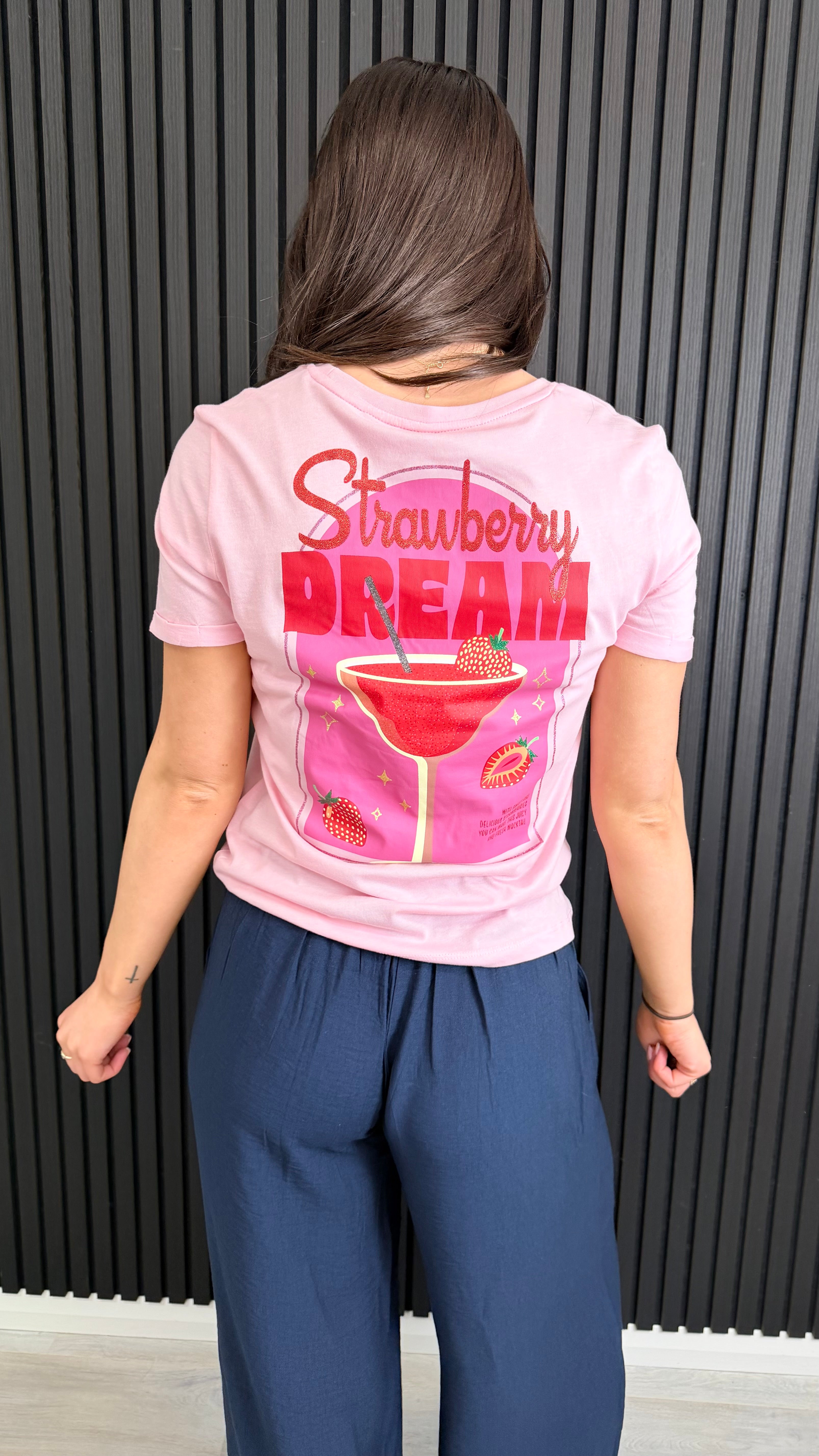 Back view of pink Strawberry Dream graphic t-shirt worn with navy trousers.