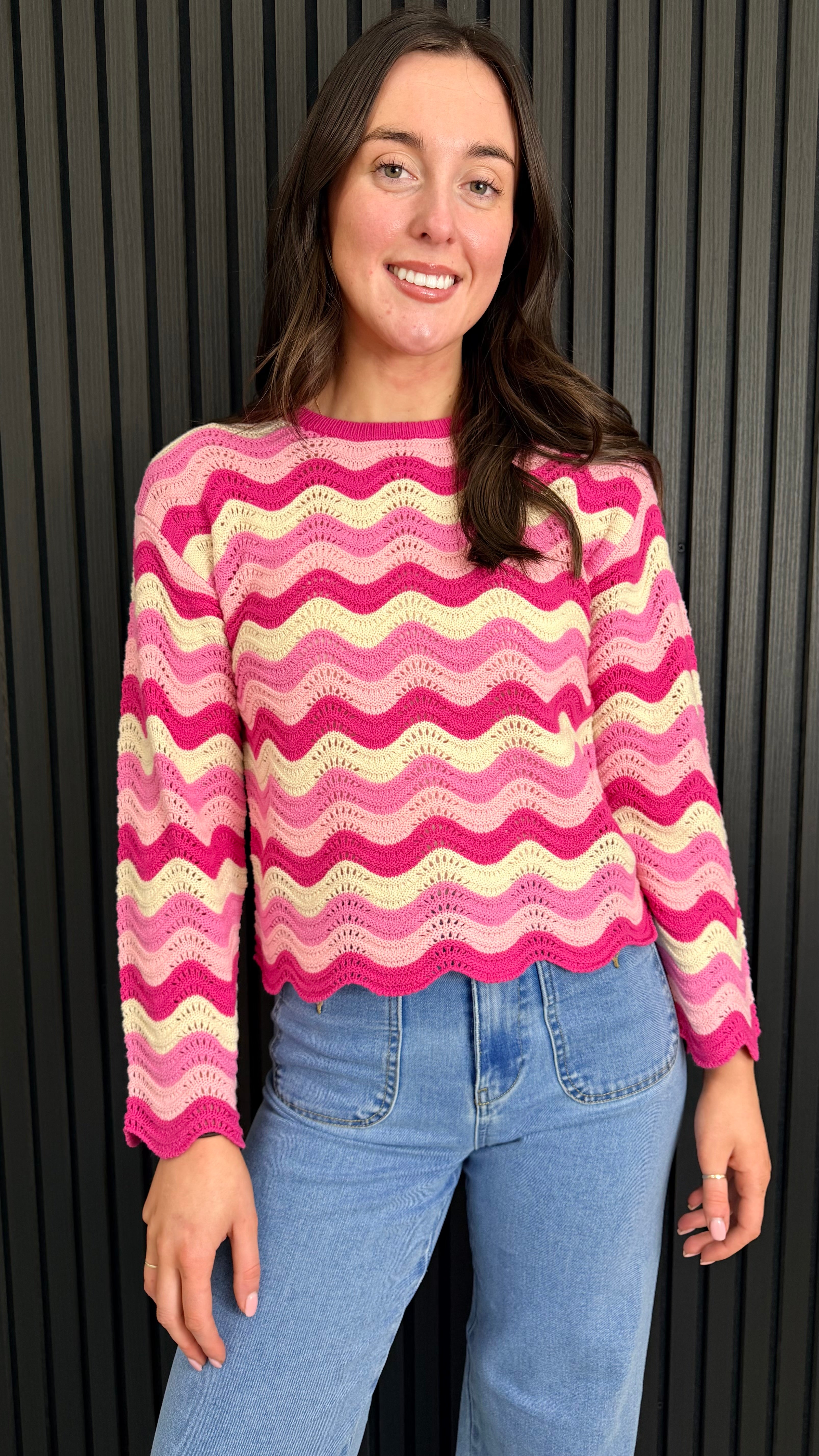 Woman wearing a pink and cream zigzag knit jumper styled with blue jeans.