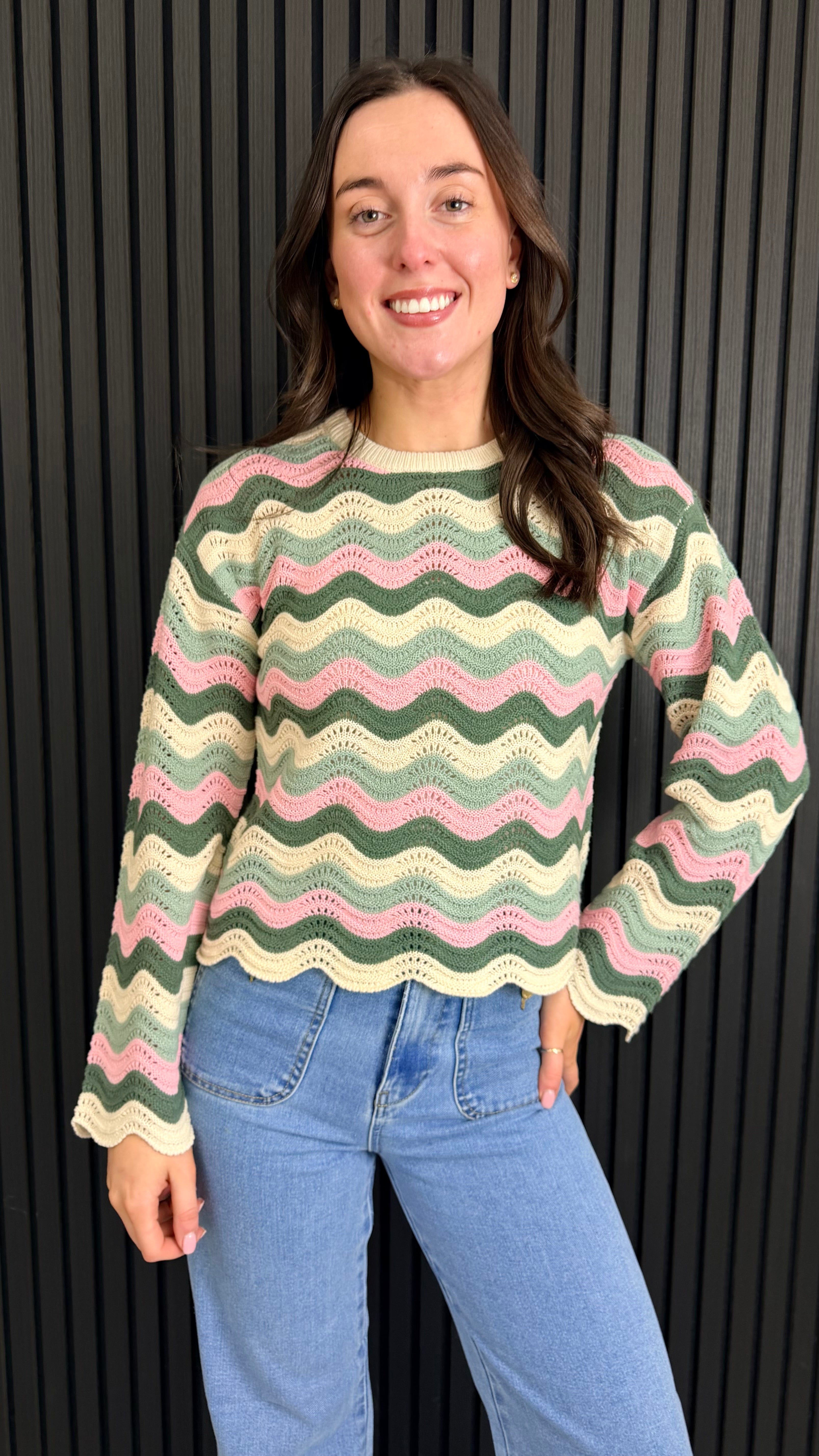 Woman wearing a pink and cream zigzag knit jumper styled with blue jeans.
