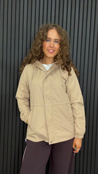Women’s lightweight hooded jacket in Humus with an adjustable waist, front zip and popper fastening, and practical side pockets.