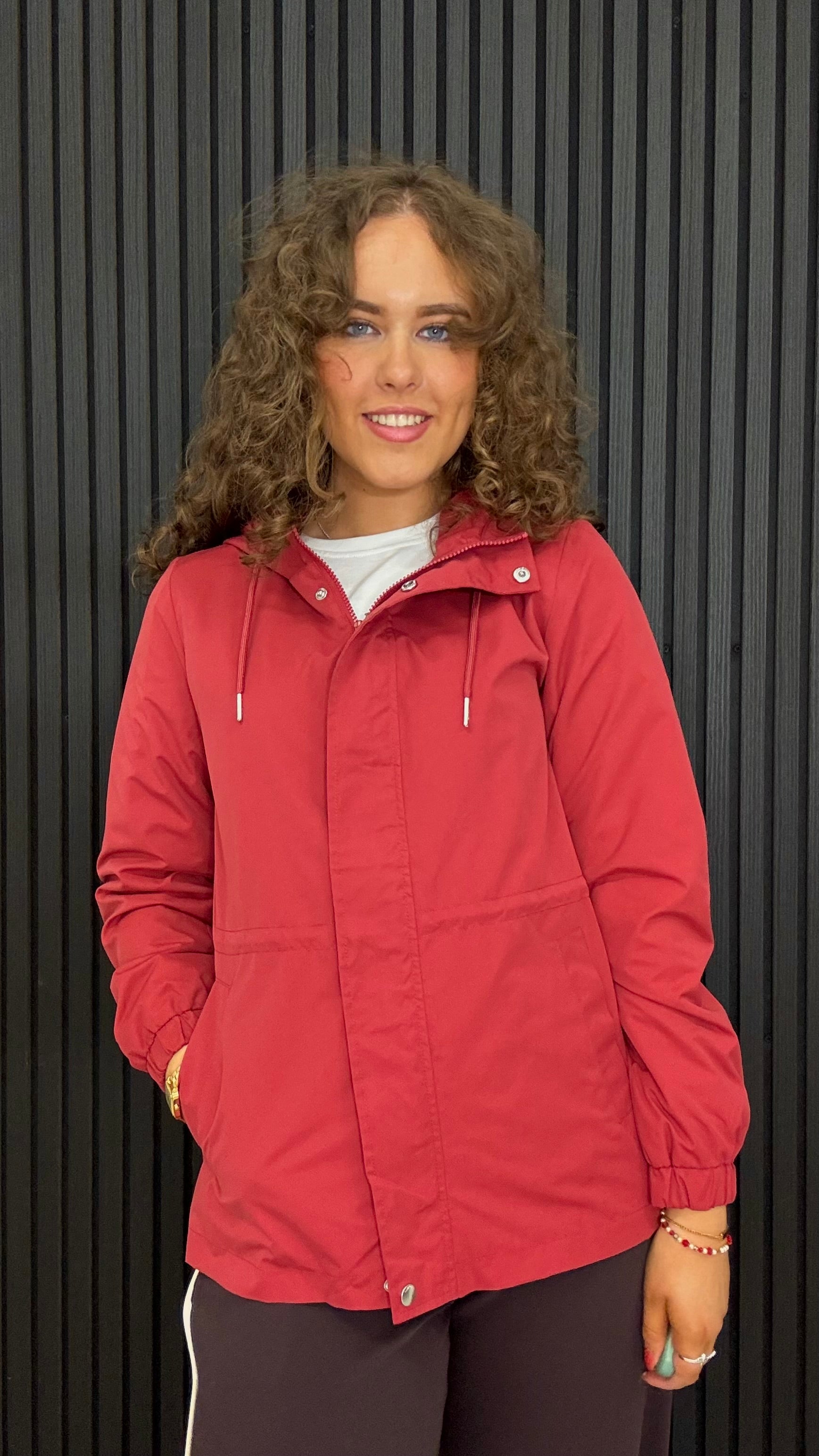 Women’s lightweight hooded jacket in red with an adjustable waist, front zip and popper fastening, and practical side pockets.