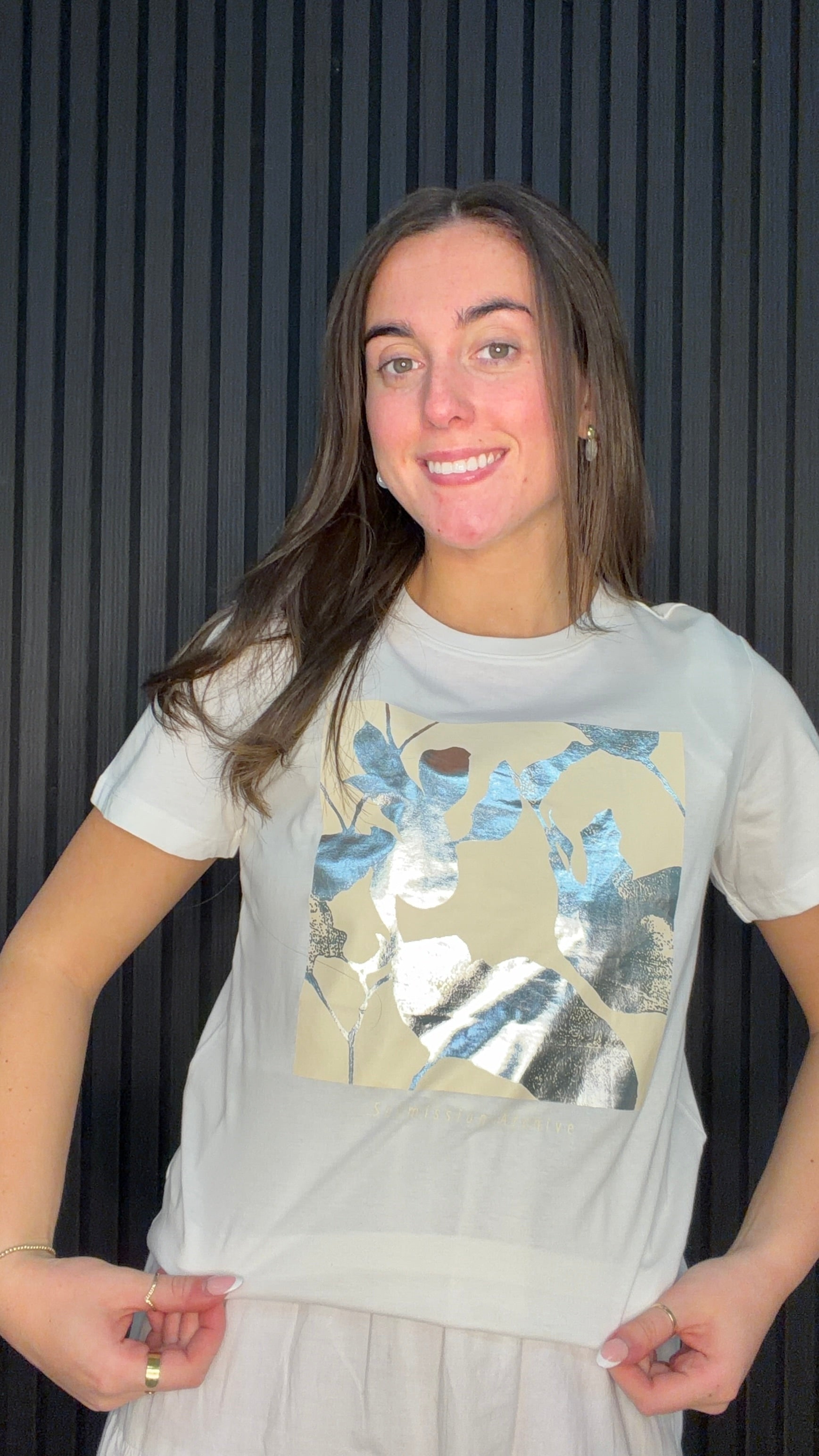 Model wearing the Lima Botanical Graphic T-Shirt in Cloud Dancer with a metallic blue and silver leaf print.